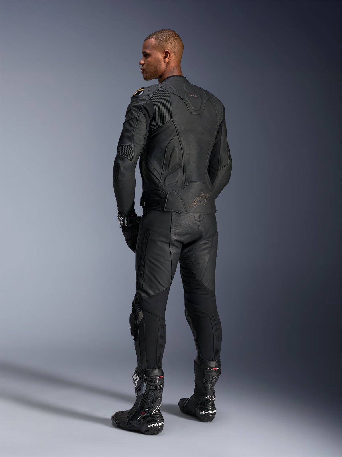 Alpinestars Dusk Leather Jacket, Motorcycle Jacket, Black Laser, rear view on a model wearing full leather racing gear, 3D multi-panel construction with laser-etched branding, premium bovine leather for sport and road riding.