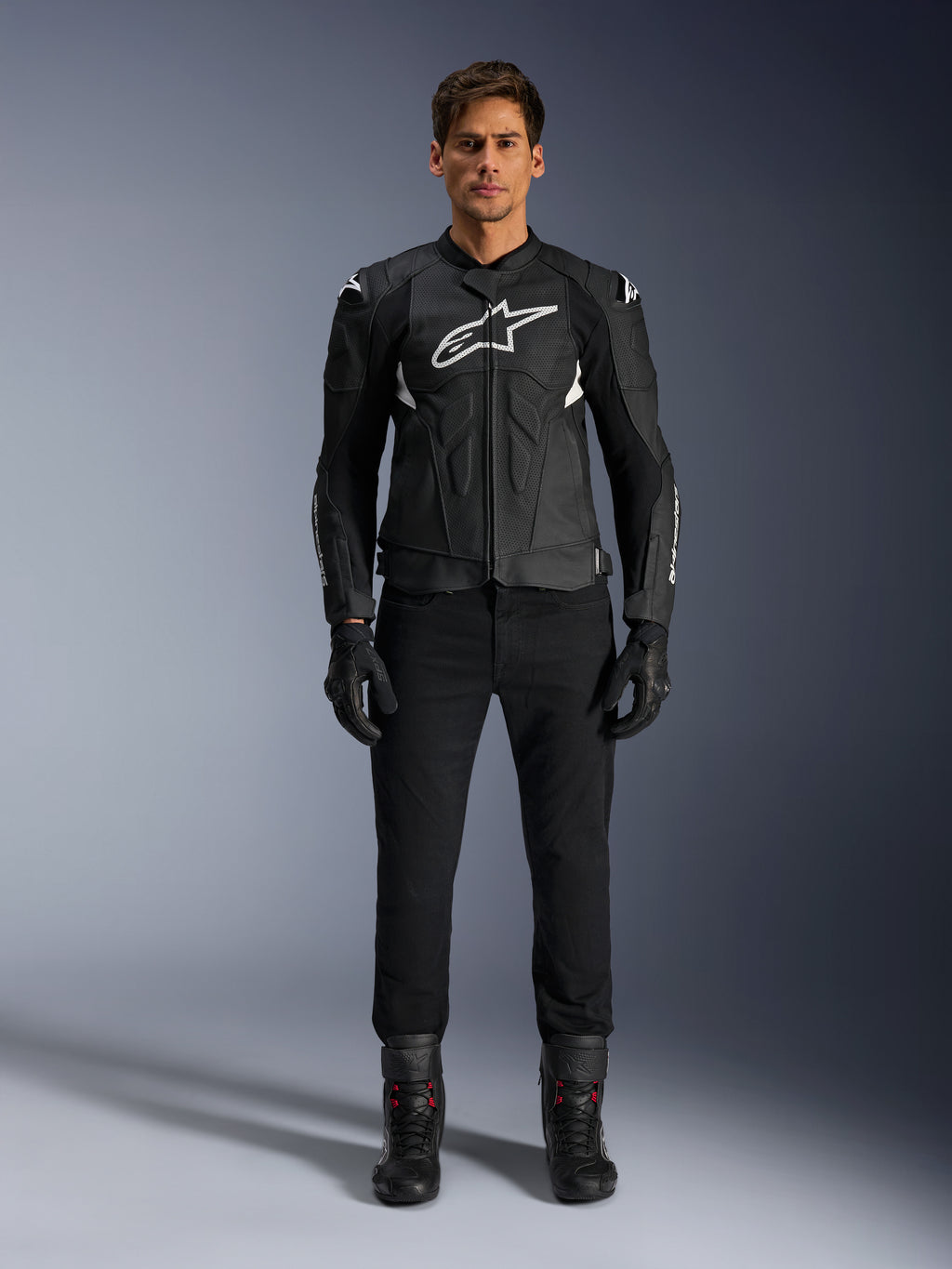 Alpinestars Dusk Airflow Lederjacke, Schwarz und Weiß, Motorrad-Lederjacke mit perforierten Paneelen für Luftzirkulation, weißes Astars-Logo auf der Brust, getragen von einem männlichen Fahrer mit schwarzer Hose, Handschuhen und Motorradstiefeln, professionelle Studioaufnahme für Sport-Motorradbekleidung.