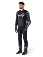 Männliches Modell in Alpinestars Faster V3 Lederjacke, Sport-Motorradjacke, Schwarz und Weiß, kombiniert mit schwarzer Motorradhose, Handschuhen und Stiefeln, mit weißen Brandings und Logos, sportliche Silhouette für den Straßenrennsport