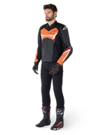 Alpinestars Faster V3 Airflow Lederjacke, Schwarz und Rot Fluo, getragen von einem männlichen Model mit schwarzer Motorradhose, Handschuhen und Rennstiefeln, mit perforiertem Leder und sportlicher Silhouette.