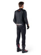 Alpinestars Faster V3 Airflow Lederjacke, Schwarz und Fluo-Rot, Rückansicht an einem Fahrer, mit perforierten Ledereinsätzen und markantem Branding, getragen mit schwarzer Hose und Motorradstiefeln, sportliche Motorradausrüstung.