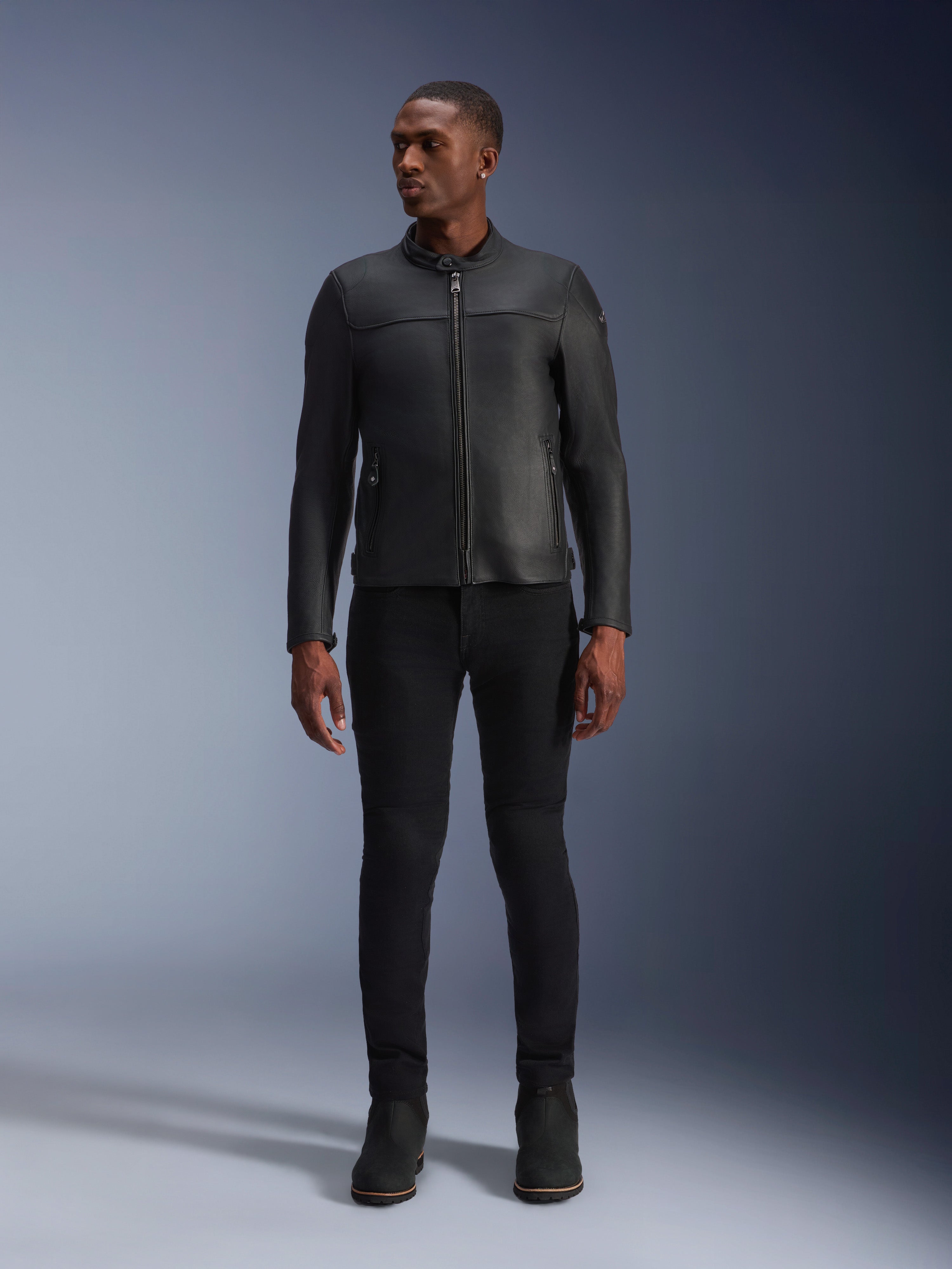 Male model wearing Alpinestars Blacktrack Leather Jacket, Black premium bovine leather, modern minimalist biker design with a tailored fit, paired with black riding pants and boots, urban contemporary style