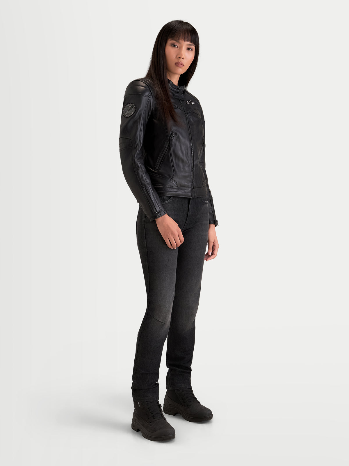 Alpinestars Revea Damen Lederjacke, urbane Motorradjacke in Schwarz, Dreiviertelansicht an Model mit dunklen Jeans und Motorradstiefeln, Vollnarbenrindleder-Konstruktion mit AA-Sicherheitszertifizierung