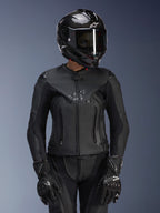 Alpinestars Damen Stella GP Plus V4 Lederjacke in Schwarz, getragen mit schwarzem Carbon-Helm und Rennhandschuhen, elegante Lederkonstruktion mit dezentem Branding auf der Brust, taillierte Silhouette für Fahrerinnen, professionelle Sport-Motorradausrüstung