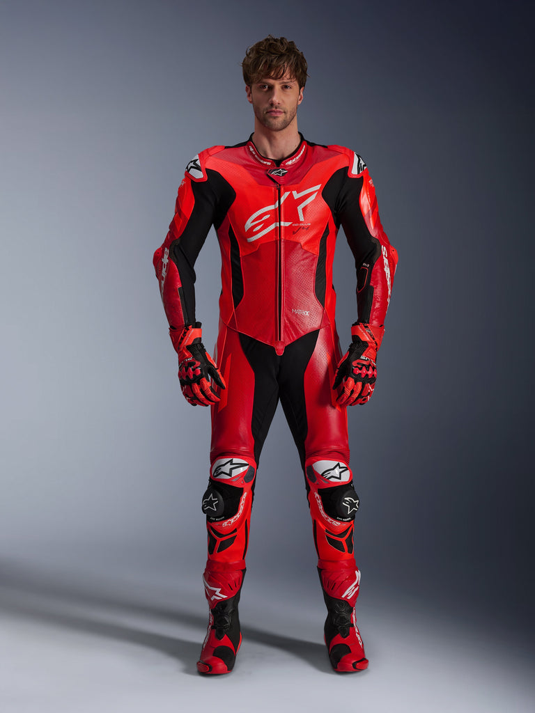 Alpinestars GP Plus V4 Sprint einteilige Lederkombi, Modell trägt die Farbkombination Red Fluo Mid Red und Weiß mit schwarzen und weißen Akzenten, kombiniert mit passenden Rennhandschuhen und Stiefeln, sportliches Design mit großem Brustlogo und perforierten Lederbahnen zur Belüftung.