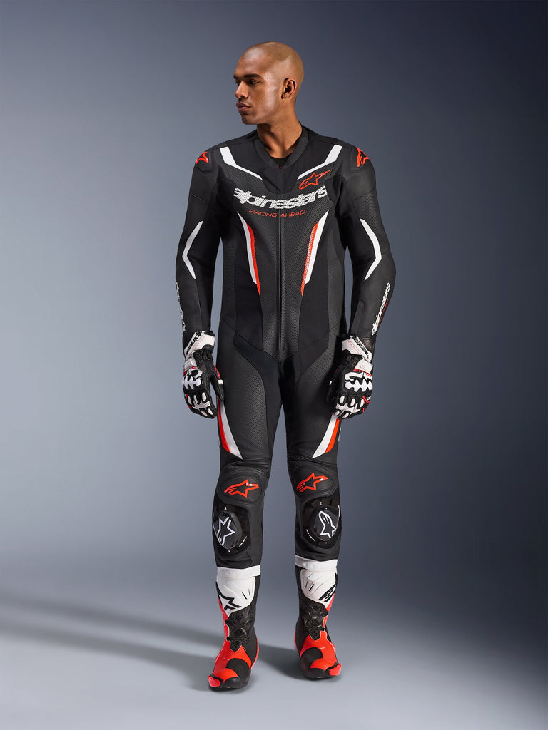 Alpinestars GP Force V2 Lederkombi – 1-Teiler, Schwarz, Weiß und Fluo-Rot, Ganzkörperansicht eines männlichen Models in professioneller Motorrad-Rennausrüstung mit passenden Handschuhen und Stiefeln, mit perforierten Lederbahnen und schützenden Knieschleifern.