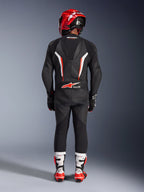 Rider viewed from behind wearing the Alpinestars GP Force V2 Leather Suit 1-Piece in Black White Red Fluo, featuring an aerodynamic speed hump and Tech-Air Ready branding, coordinated with a red racing helmet and white and red boots, professional track gear design.