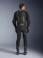 Rear view of the Alpinestars GP Force V2 1-Piece Leather Suit in Black and Green, featuring an aerodynamic speed hump, perforated panels, and Tech-Air Ready branding on the lower back, worn with black racing gloves and boots.