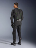 Alpinestars GP Force V2 Leather Suit, 1-Piece Motorcycle Suit, Black with Green accents, back view showing the aerodynamic speed hump and white logo on the accordion stretch panel, paired with black racing boots and gloves.