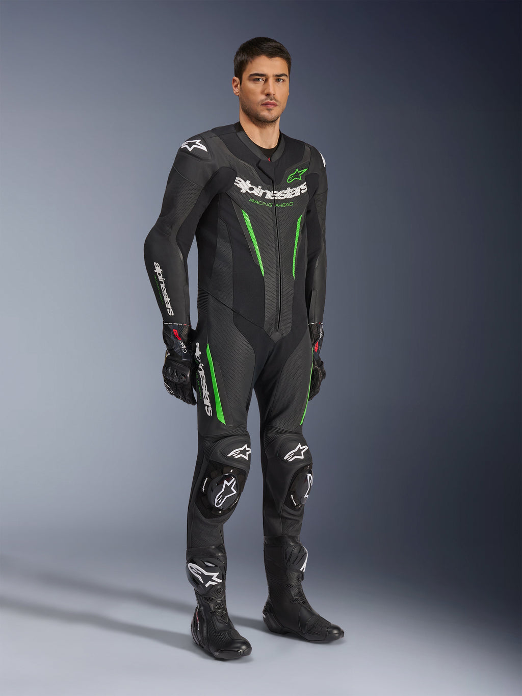 Alpinestars GP Force V2 Leather Suit 1-Piece, Black and Green, full racing gear worn with black gloves and boots, featuring perforated leather panels, white Alpinestars branding, and integrated knee sliders, professional track performance suit