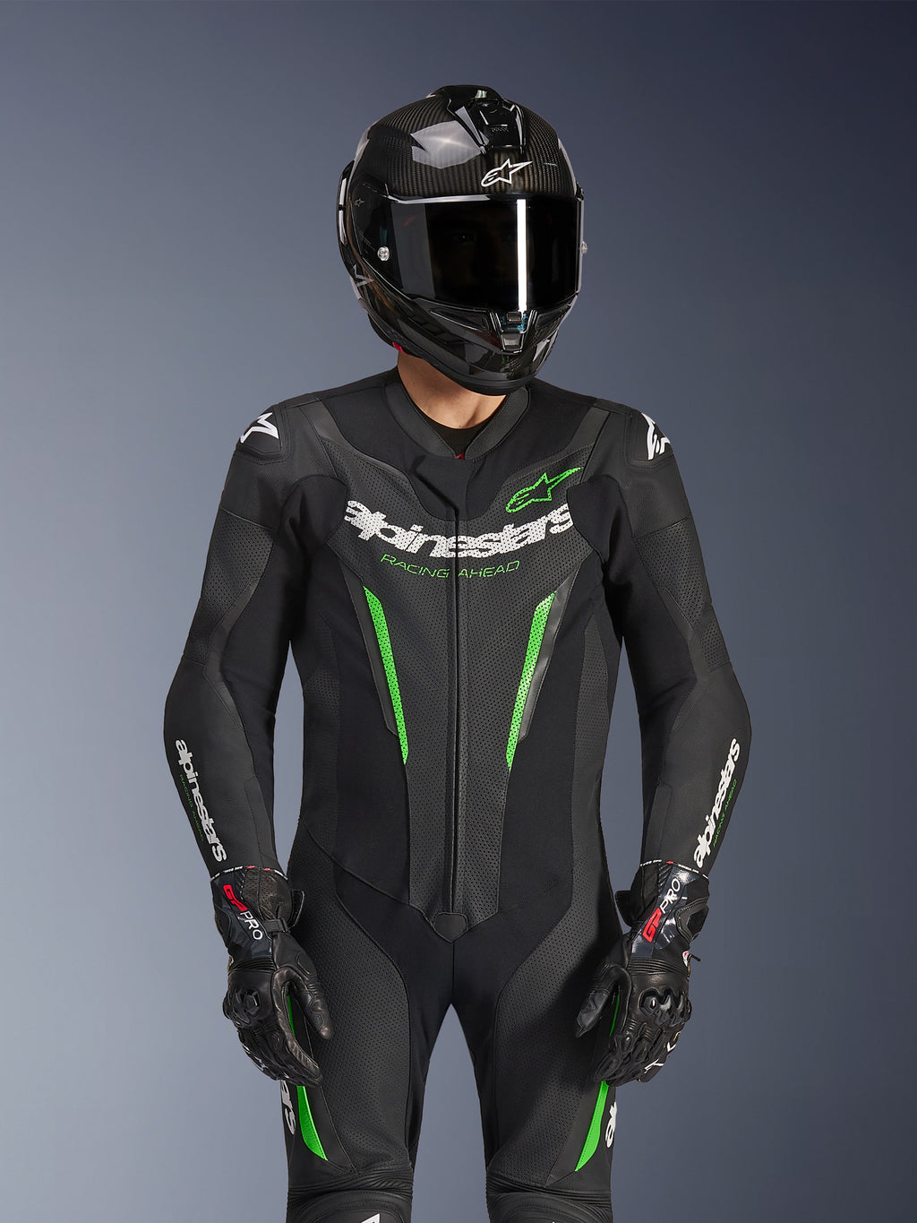 Alpinestars GP Force V2 Leather Suit - 1Piece, Black and Green, motorcycle racing suit worn with a carbon fiber helmet and GP Pro gloves, featuring lime green accents and Alpinestars 'Racing Ahead' branding, engineered for track performance.