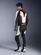 Motorcycle rider wearing the Alpinestars GP Force V2 Leather Suit - 1Piece in White Black and Red Fluo, rear-side view showing the aerodynamic speed hump and perforated leather panels, paired with matching racing boots and gloves, designed for track and performance riding.