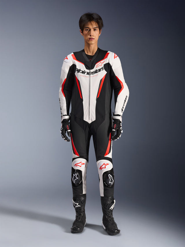 Alpinestars GP Force V2 Lederkombi - 1-teilig, Weiß Schwarz Rot Fluo, einteiliger Motorrad-Lederkombi, Vorderansicht am Modell, mit perforierten Einsätzen und roten Akzenten, markantes Alpinestars-Branding auf der Brust, kombiniert mit professionellen Rennstiefeln und Handschuhen