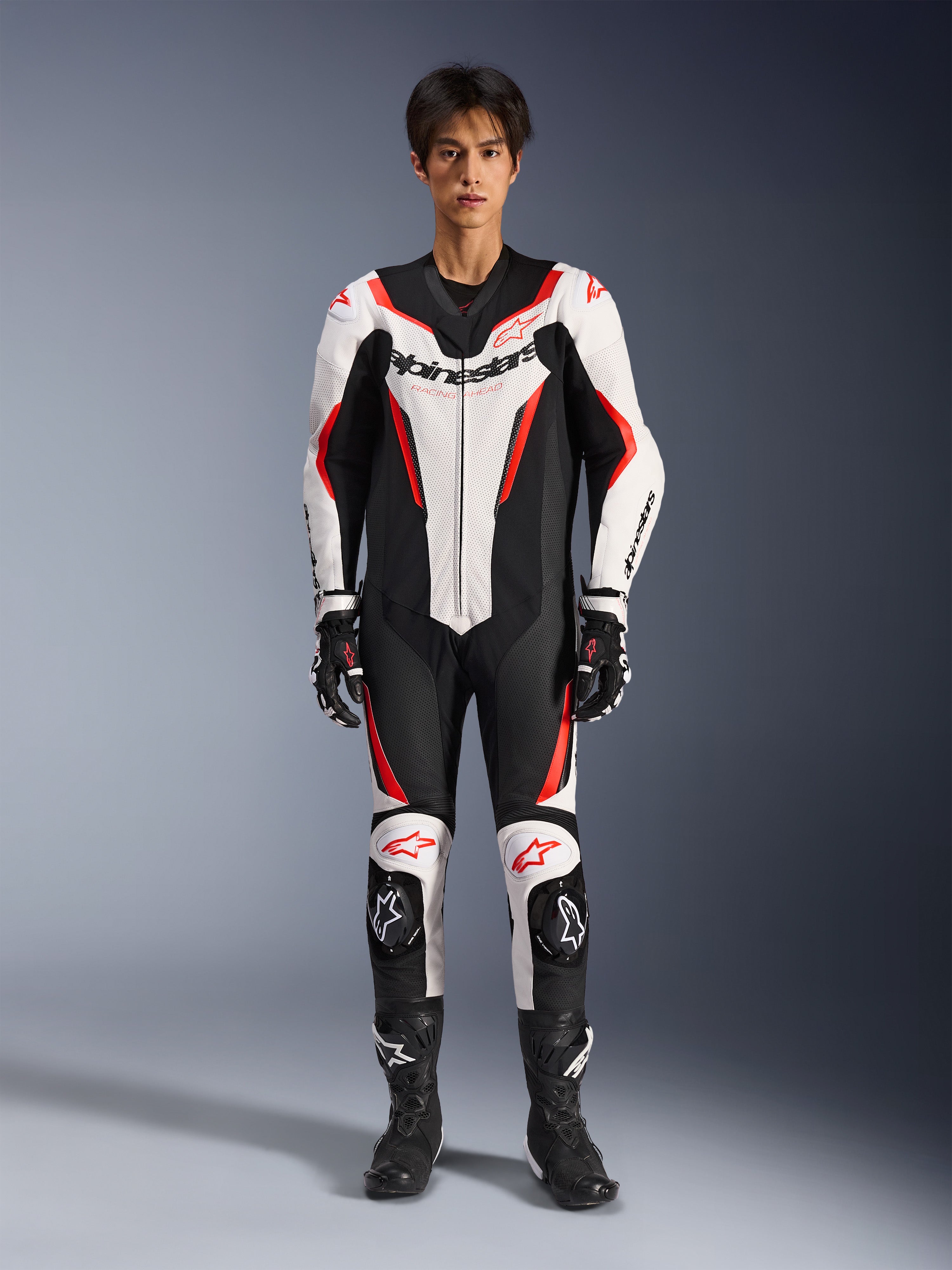 Alpinestars GP Force V2 Leather Suit - 1Piece, White Black and Red Fluo, one-piece motorcycle racing suit, worn by model with matching racing gloves and boots, featuring bold Alpinestars branding, perforated leather panels, and aerodynamic sport design