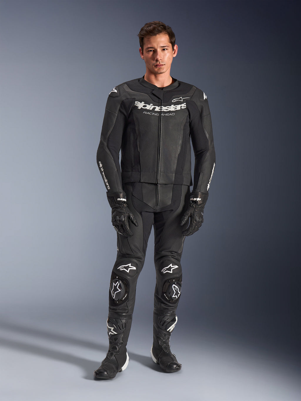 Alpinestars GP Force V2 Leather Suit 2-Piece, Black with white logos, full-body motorcycle racing suit, featuring premium leather construction with reinforced knee sliders and perforated panels, worn with black gloves and boots, studio full-length view