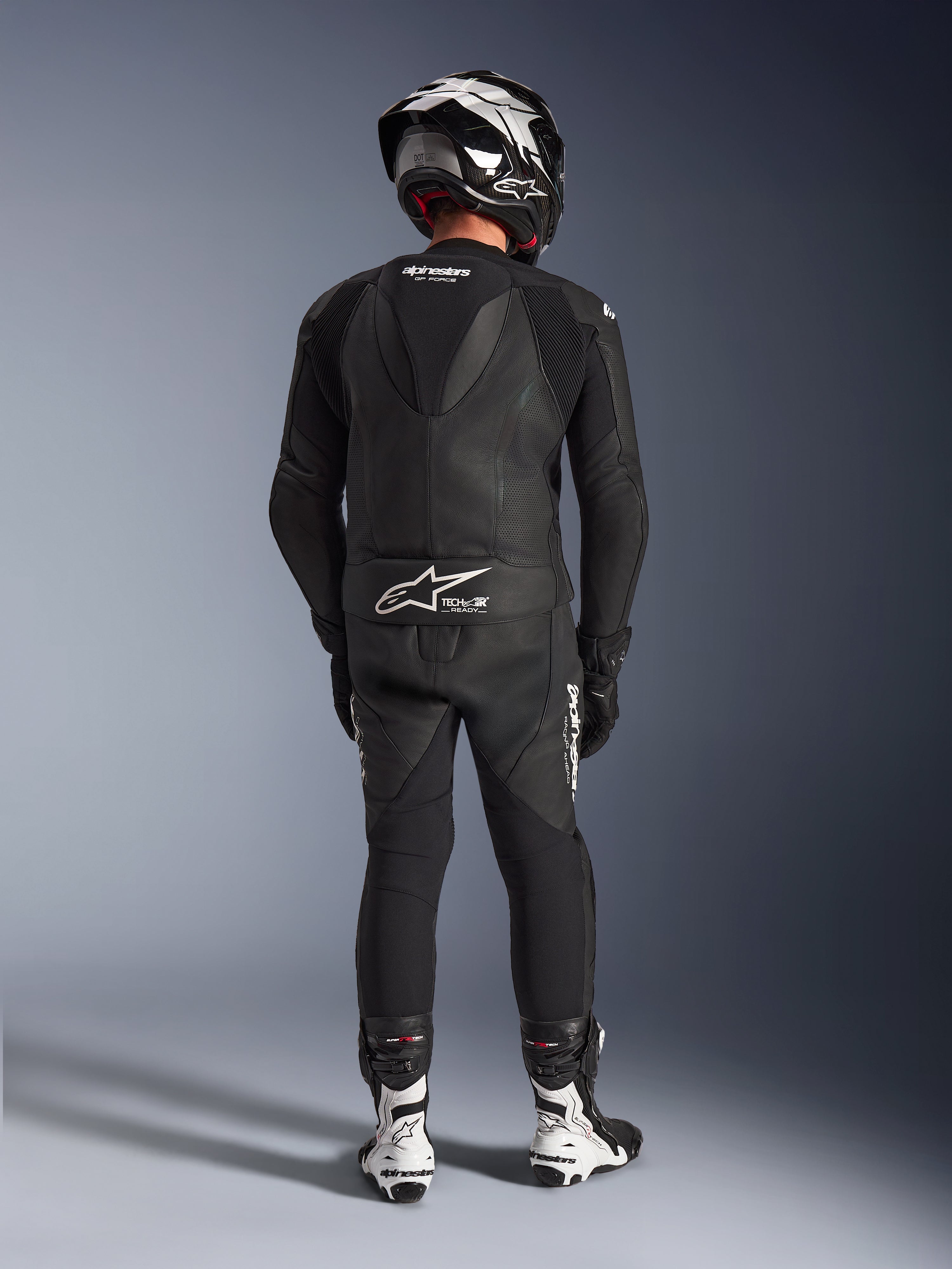 Alpinestars GP Force V2 2-Piece Leather Suit in Black, full rear view showing aerodynamic speed hump and Tech-Air Ready branding, paired with matching black and white helmet and white racing boots for professional track performance