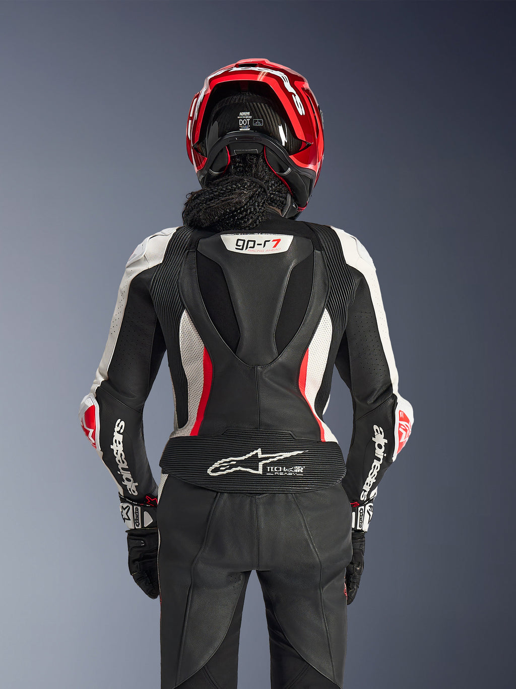 Alpinestars Woman Stella GP-R7 2-Piece Leather Suit, Black White and Red Fluo, back view of a rider wearing a red helmet and black gloves, featuring an aerodynamic hump with gp-r7 branding and Tech-Air Ready logo on the lower back.
