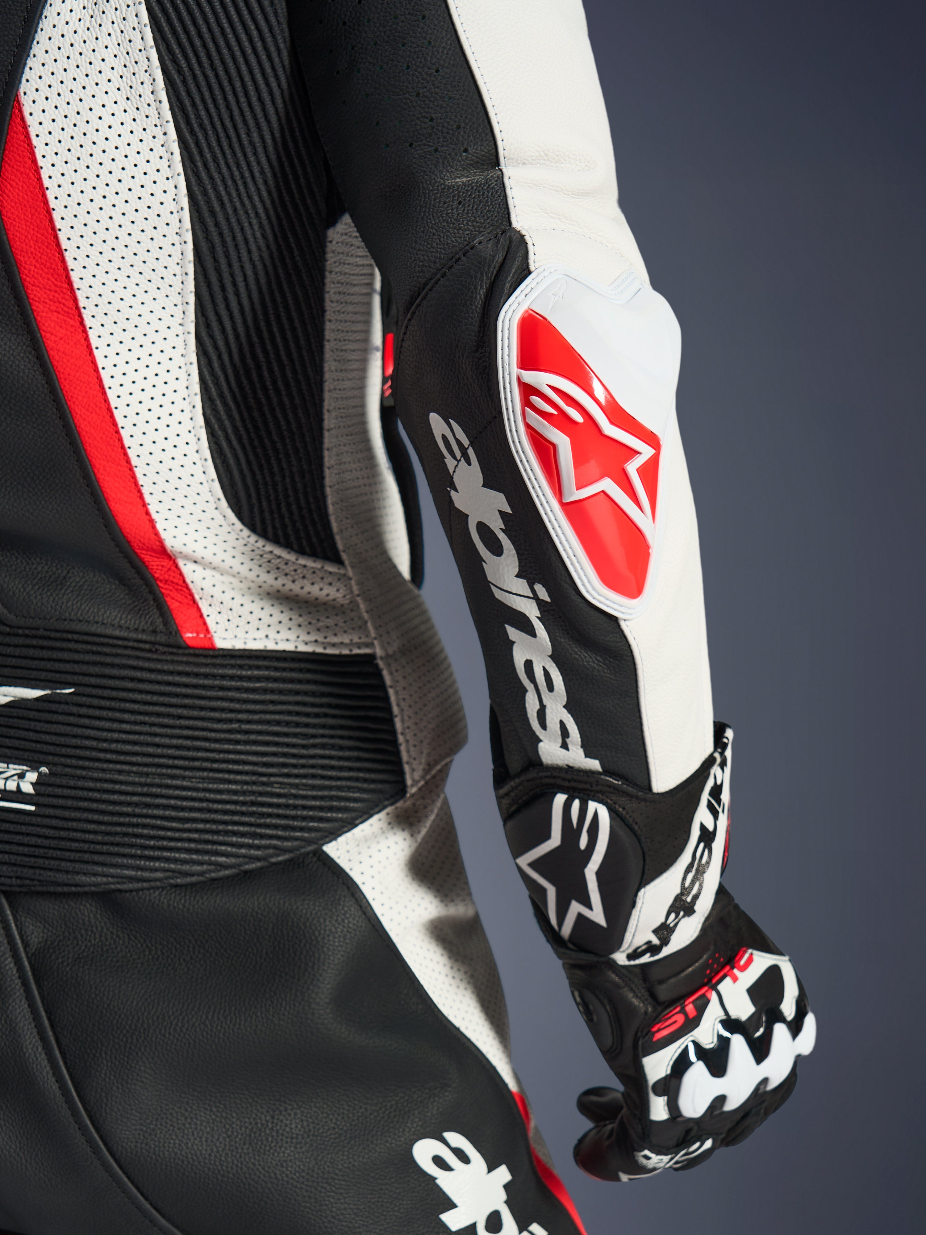 Close-up of the Alpinestars Woman Stella GP-R7 2-Piece Leather Suit, Black White and Red Fluo, featuring the GP DFS RR elbow slider with a red star logo, white Alpinestars wordmark on the forearm, and detailed perforated leather and accordion stretch panels.