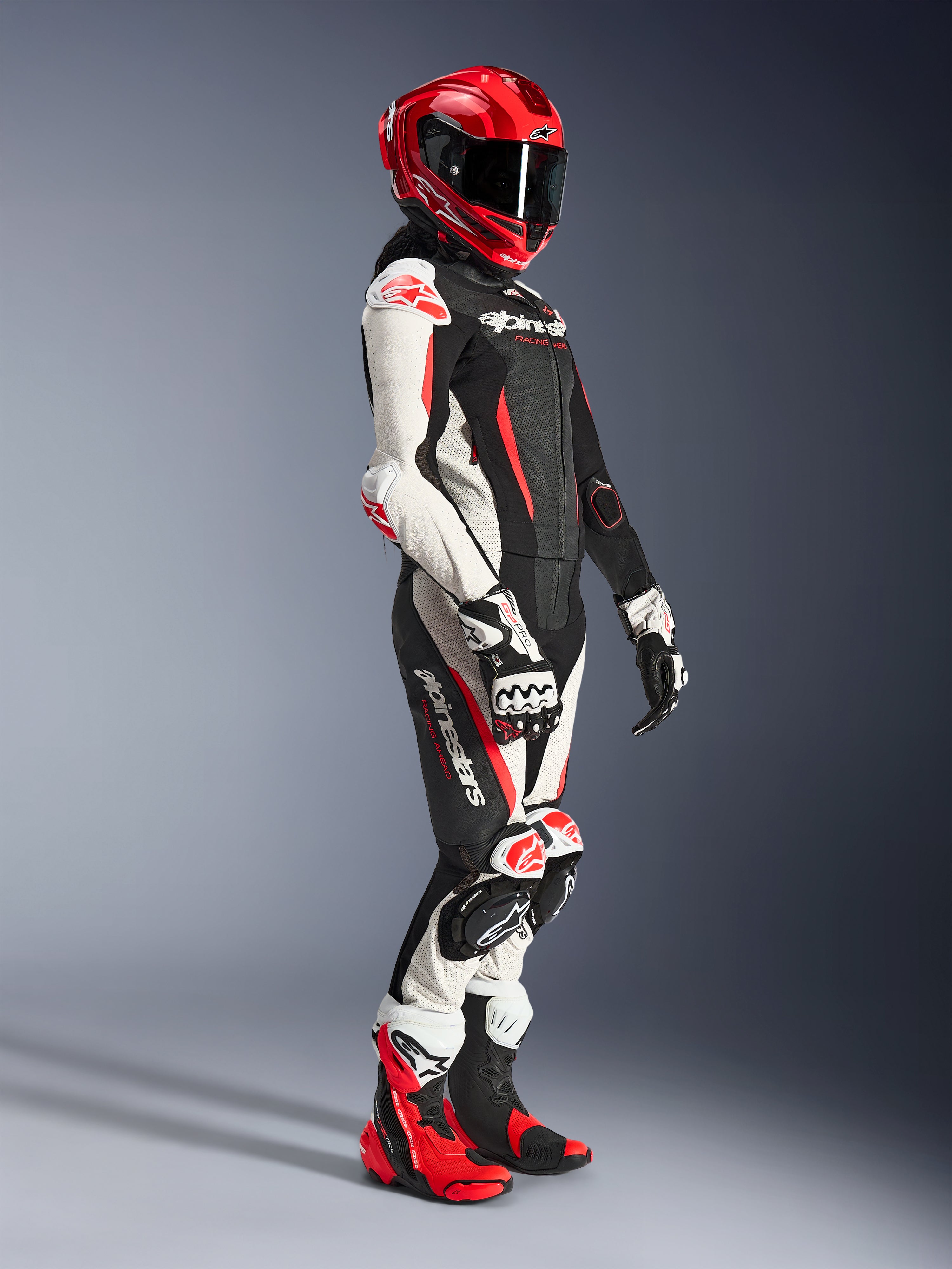 Woman rider wearing the Alpinestars Stella GP-R7 2-Piece Leather Suit in Black, White, and Red Fluo, styled with a red full-face racing helmet, matching gloves, and performance boots, professional motorcycle racing gear for women.