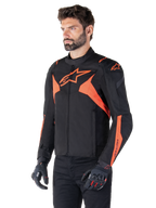 Alpinestars T-Jaws V4 Waterproof Jacket, Black and Red Fluo, sport motorcycle jacket worn by a male model, featuring prominent orange star logos on the chest and shoulders, paired with black gloves and pants