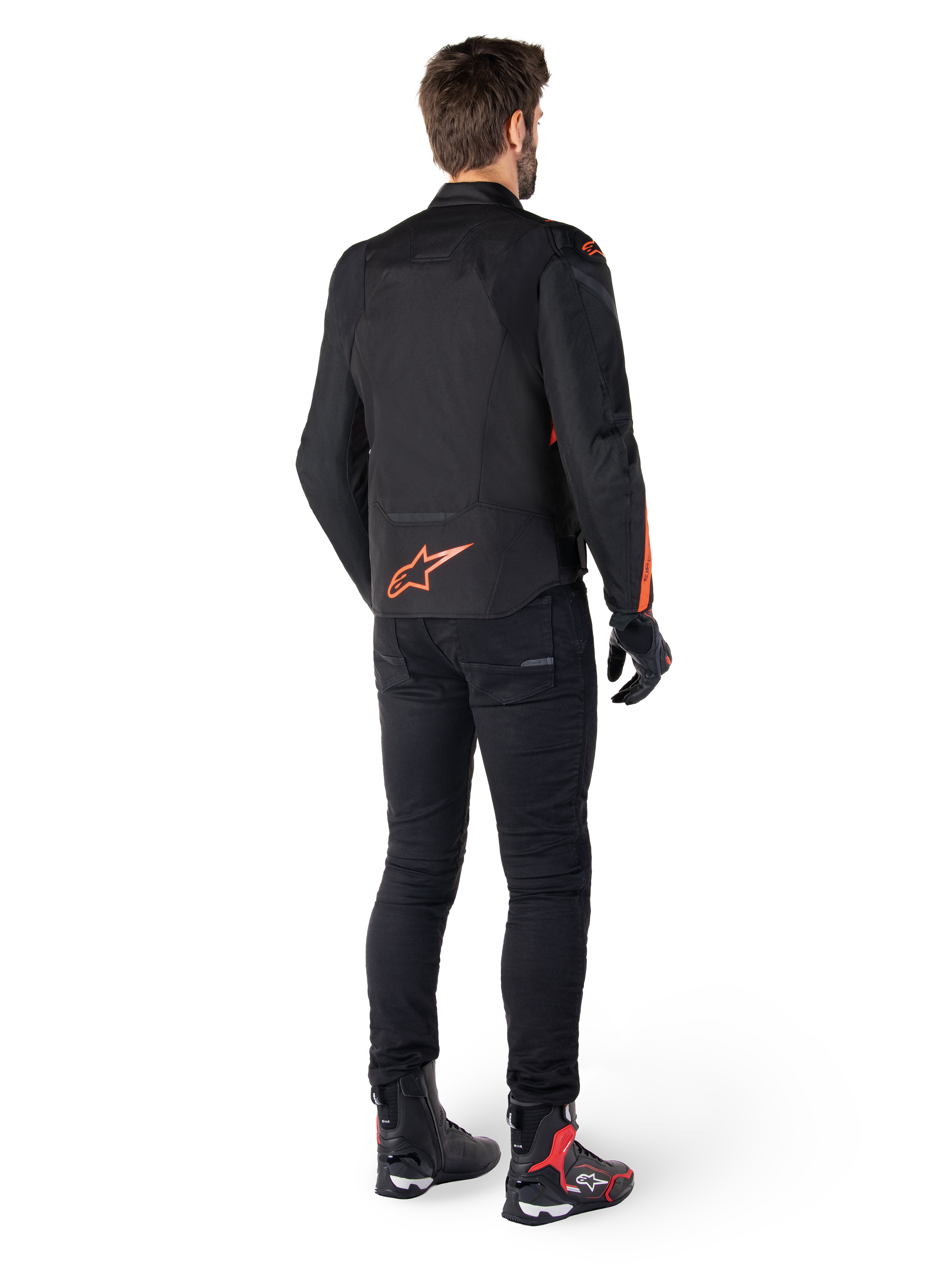 Alpinestars T-Jaws V4 Waterproof Jacket, Black and Red Fluo, rear view worn by a male rider, featuring a vibrant red fluo logo on the back, styled with black riding pants and technical boots, sport motorcycle apparel.