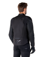 Alpinestars T-Jaws V4 Waterproof Jacket, Black, back view on model, featuring a reflective Alpinestars logo on the lower back, extended rear for coverage, sporty textile design with tonal panels, worn with black motorcycle gloves