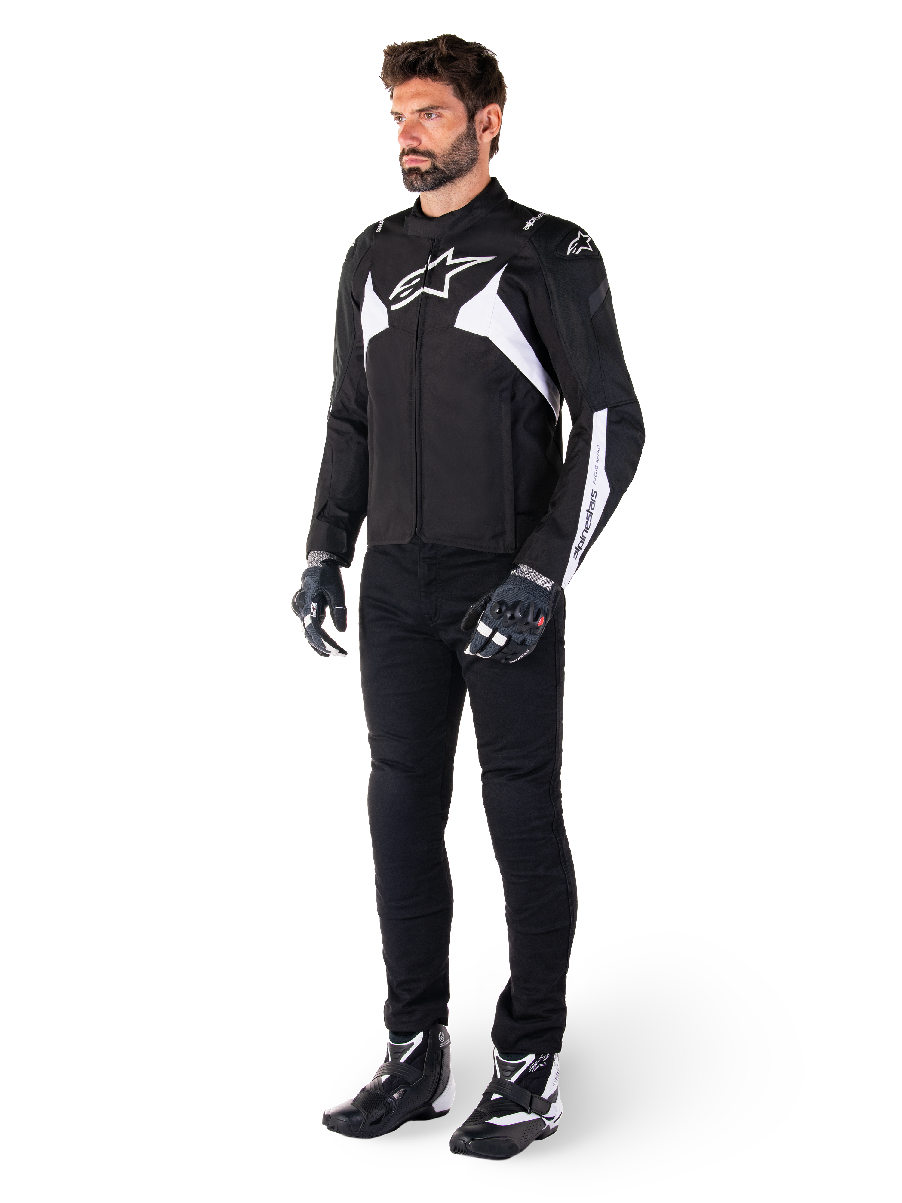 Male model wearing Alpinestars T-Jaws V4 Waterproof Jacket in Black and White, sport textile jacket featuring a white star logo and sleeve accents, styled with black motorcycle pants, gloves, and boots for a complete road riding look.