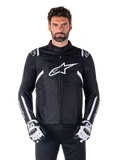 Alpinestars T-SPS V2 Waterproof Jacket in Schwarz und Weiß, Vorderansicht am Modell, wasserdichte Textil-Motorradjacke mit weißen Schulter- und Armstreifen, großes weißes Alpinestars-Logo auf der Brust, getragen mit Motorrad-Schutzhandschuhen, schlanke sportlich inspirierte Silhouette.
