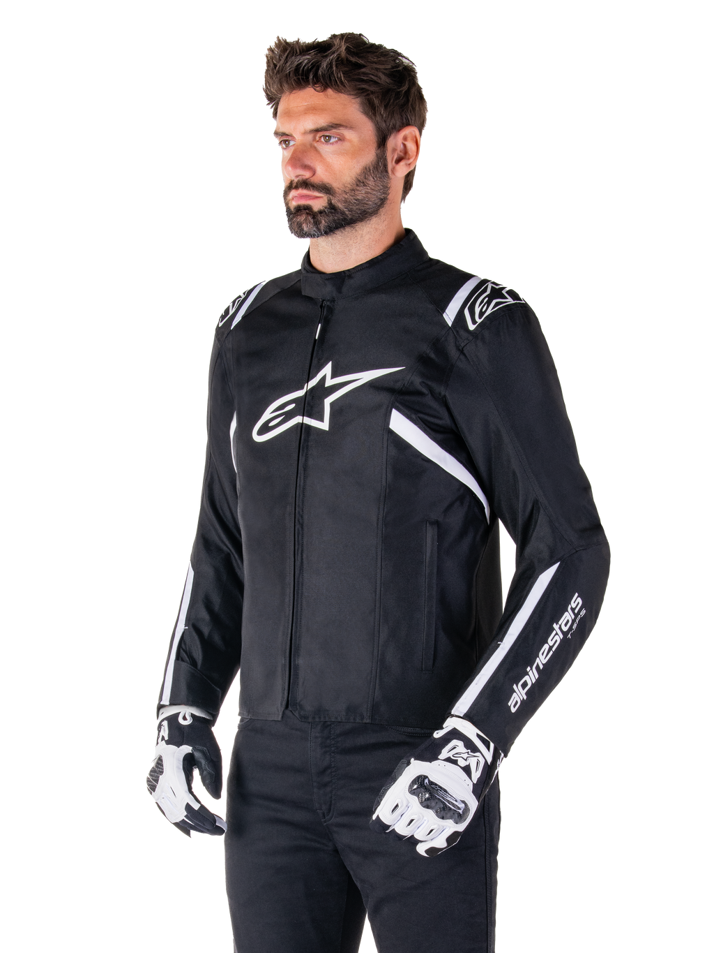 Alpinestars T-SPS V2 Waterproof Jacke, Schwarz und Weiß, getragen von einem männlichen Model mit passenden Motorradhandschuhen, Textiljacke im Sportschnitt mit weißen Alpinestars-Logos auf Brust und Schultern, „alpinestars T-SPS“-Branding am Ärmel, elegante vom Rennsport inspirierte Motorradausrüstung