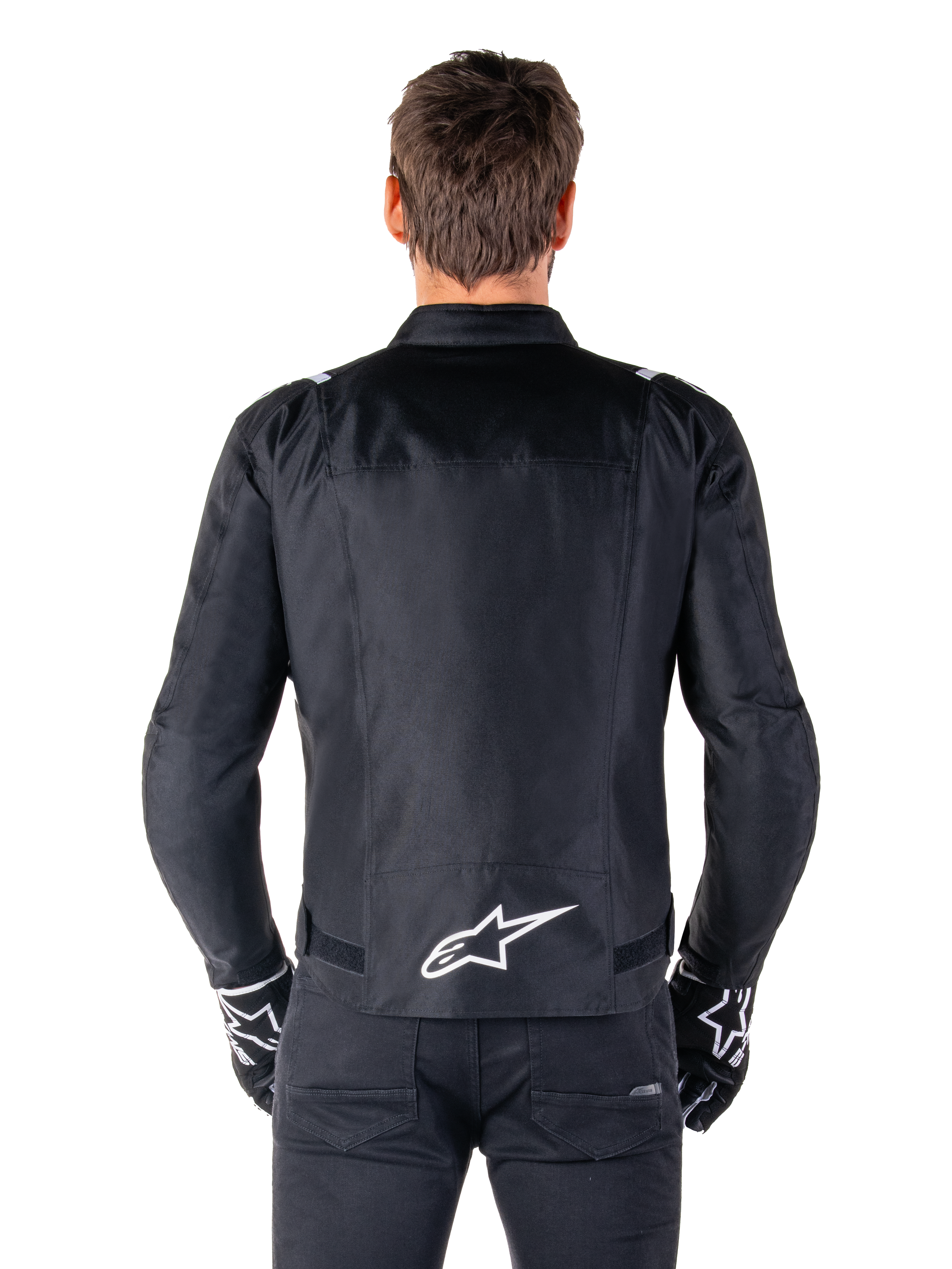Alpinestars T-SPS V2 Wasserdichte Jacke, Schwarz und Weiß, Rückansicht mit weißem Alpinestars-Logo auf dem unteren Rücken, getragen mit schwarzer Hose und Handschuhen, sportlich geschnittene Textil-Motorradjacke