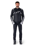 Alpinestars T-SPS V2 wasserdichte Jacke, Schwarz und Weiß, getragen von männlichem Model mit schwarzer Hose und passenden Handschuhen, weißes Alpinestars-Logo auf der Brust und Akzente an den Ärmeln, sportliche Silhouette für Allwetter-Motorradfahrten