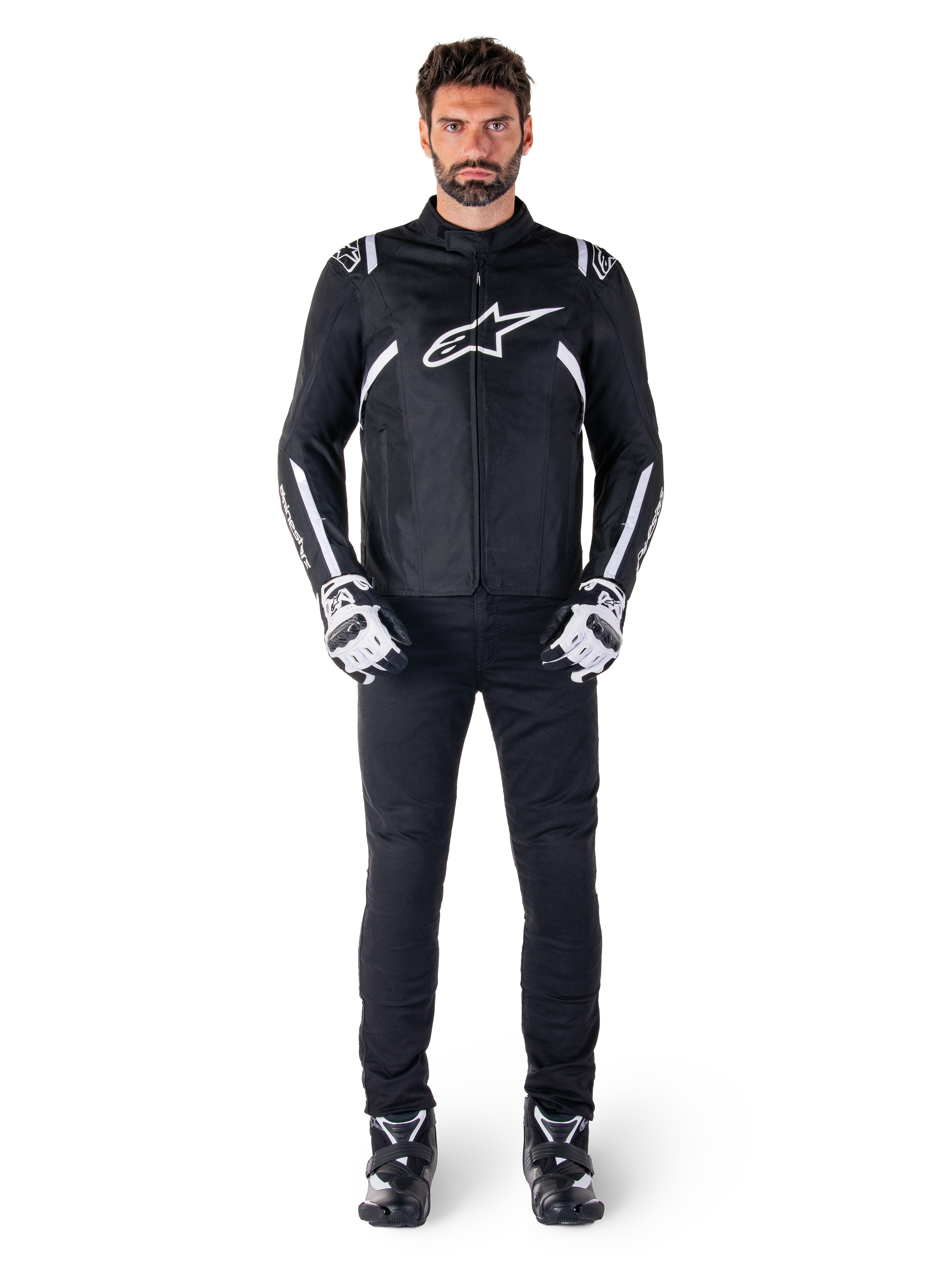 Alpinestars T-SPS V2 wasserdichte Jacke, Schwarz und Weiß, getragen von männlichem Model mit schwarzer Hose und passenden Handschuhen, weißes Alpinestars-Logo auf der Brust und Akzente an den Ärmeln, sportliche Silhouette für Allwetter-Motorradfahrten