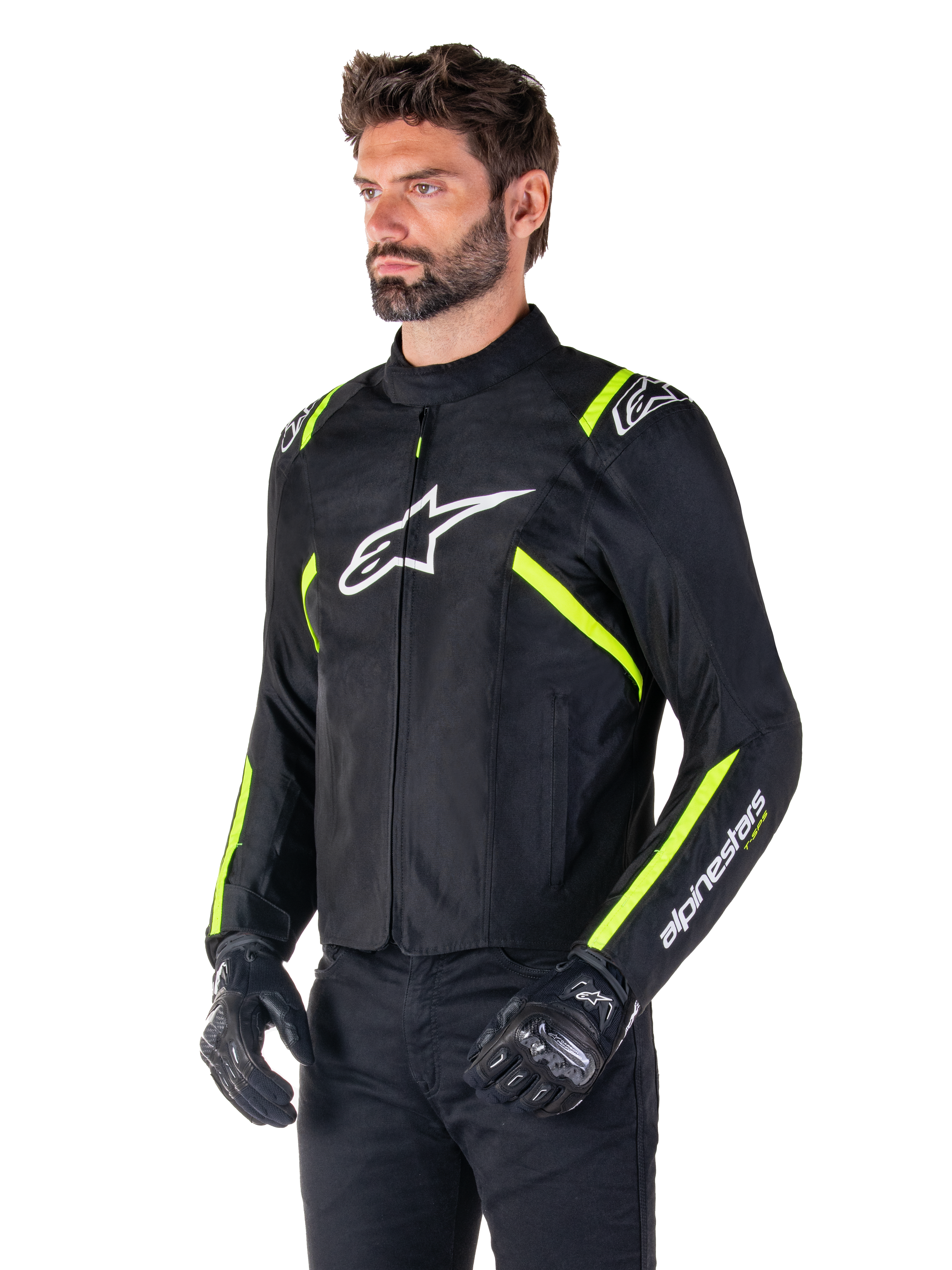 Male model wearing the Alpinestars T-SPS V2 Waterproof Jacket, Black with White and Yellow Fluo accents, featuring a white Astars logo on the chest and fluorescent yellow stripes on the shoulders and sleeves, paired with black pants and riding gloves, sport-cut textile motorcycle jacket.