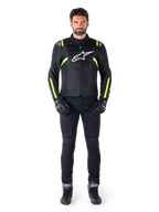 Alpinestars T-SPS V2 Waterproof Jacket, Black White and Yellow Fluo, worn by a model with black riding pants and gloves, featuring a white Alpinestars logo on the chest and fluorescent accents on shoulders and sleeves, sport-cut motorcycle gear
