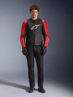 Male model wearing the Alpinestars T-SPS V2 Waterproof Jacket, Black with Red and Red Fluo sleeves, white logo on chest, paired with black pants, black riding gloves and shoes, sporty motorcycle road gear design