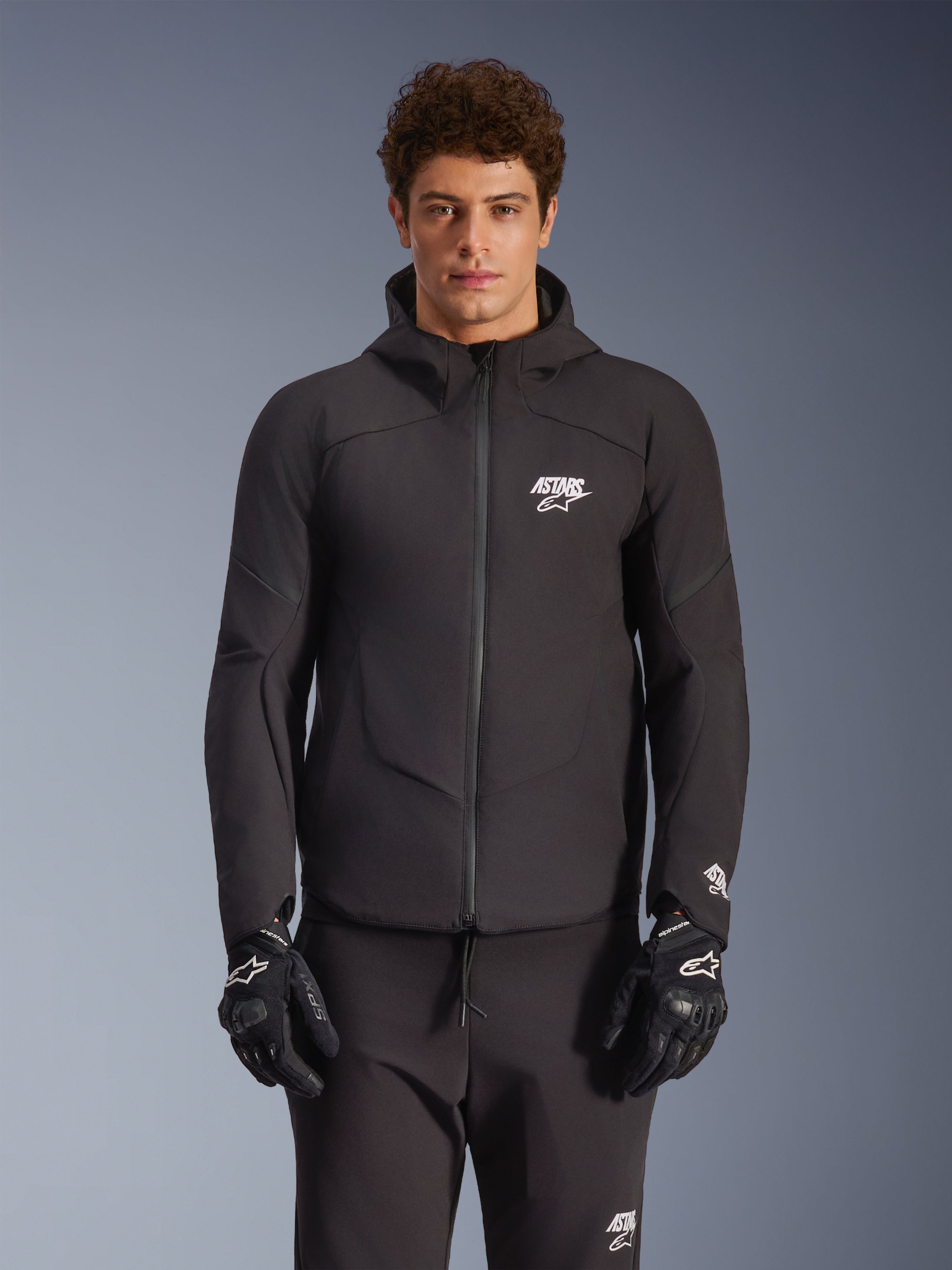 Alpinestars Aeroshell Waterproof Jacket, Black, Motorcycle Urban Jacket, Hooded Design with Full Front Zipper, White Logos on Chest and Sleeves, Worn with Matching Black Pants and Gloves