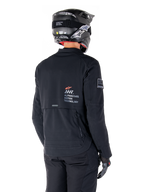 Rear view of a rider wearing the Alpinestars AMT-8 Stretch Drystar® XF Jacket in Black, featuring 'AMT Alpinestars Motion Technology' branding on the back, technical zippered ventilation, paired with a black motorcycle helmet and gloves