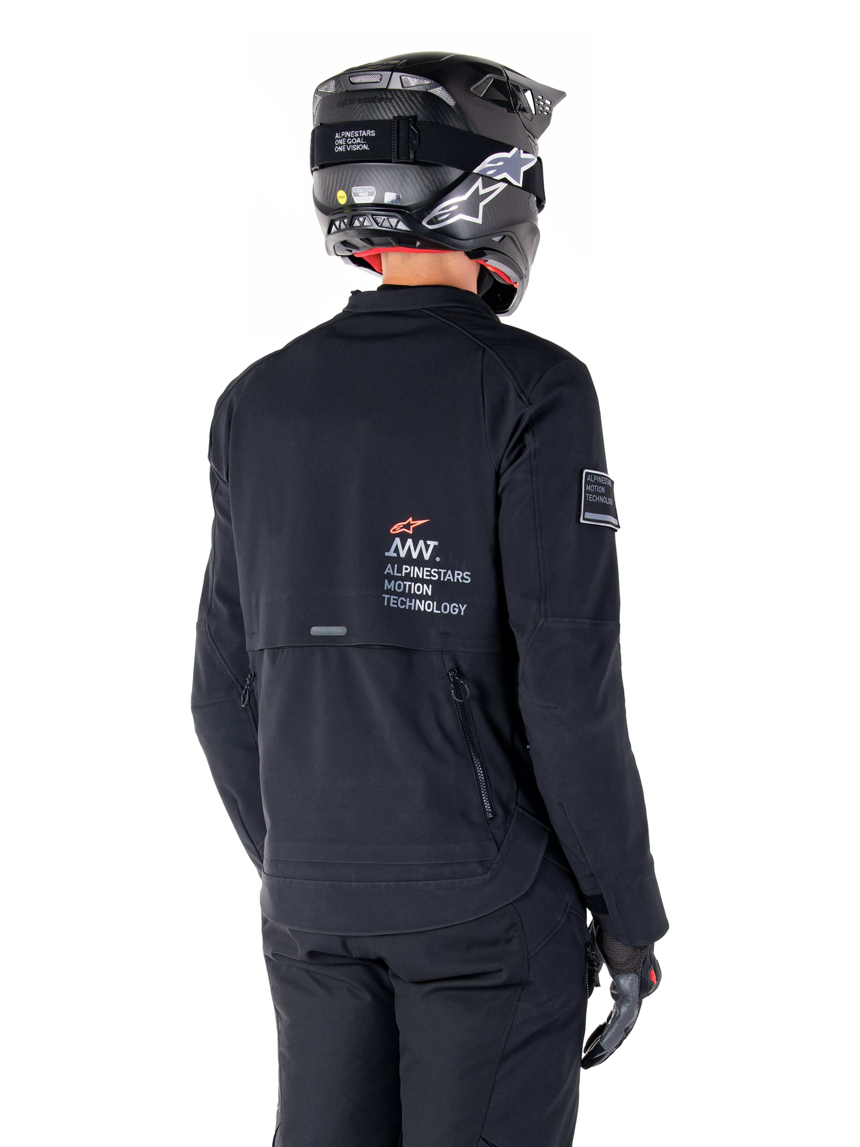 Rear view of a rider wearing the Alpinestars AMT-8 Stretch Drystar® XF Jacket in Black, featuring 'AMT Alpinestars Motion Technology' branding on the back, technical zippered ventilation, paired with a black motorcycle helmet and gloves