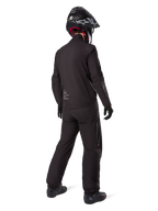 Rear view of a rider wearing the Alpinestars AMT-8 Stretch Drystar® XF Jacket liner, Black technical motorcycle gear, worn with matching pants and black helmet, featuring "AMT Alpinestars Motion Technology" branding on the back, sleek minimalist design for adventure touring