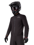 Rider wearing the Alpinestars AMT-8 Stretch Drystar® XF Liner, black windproof and waterproof stretch jacket, featuring AMT logo on the chest and Drystar XF branding on the sleeve, paired with a black adventure helmet and protective gloves.