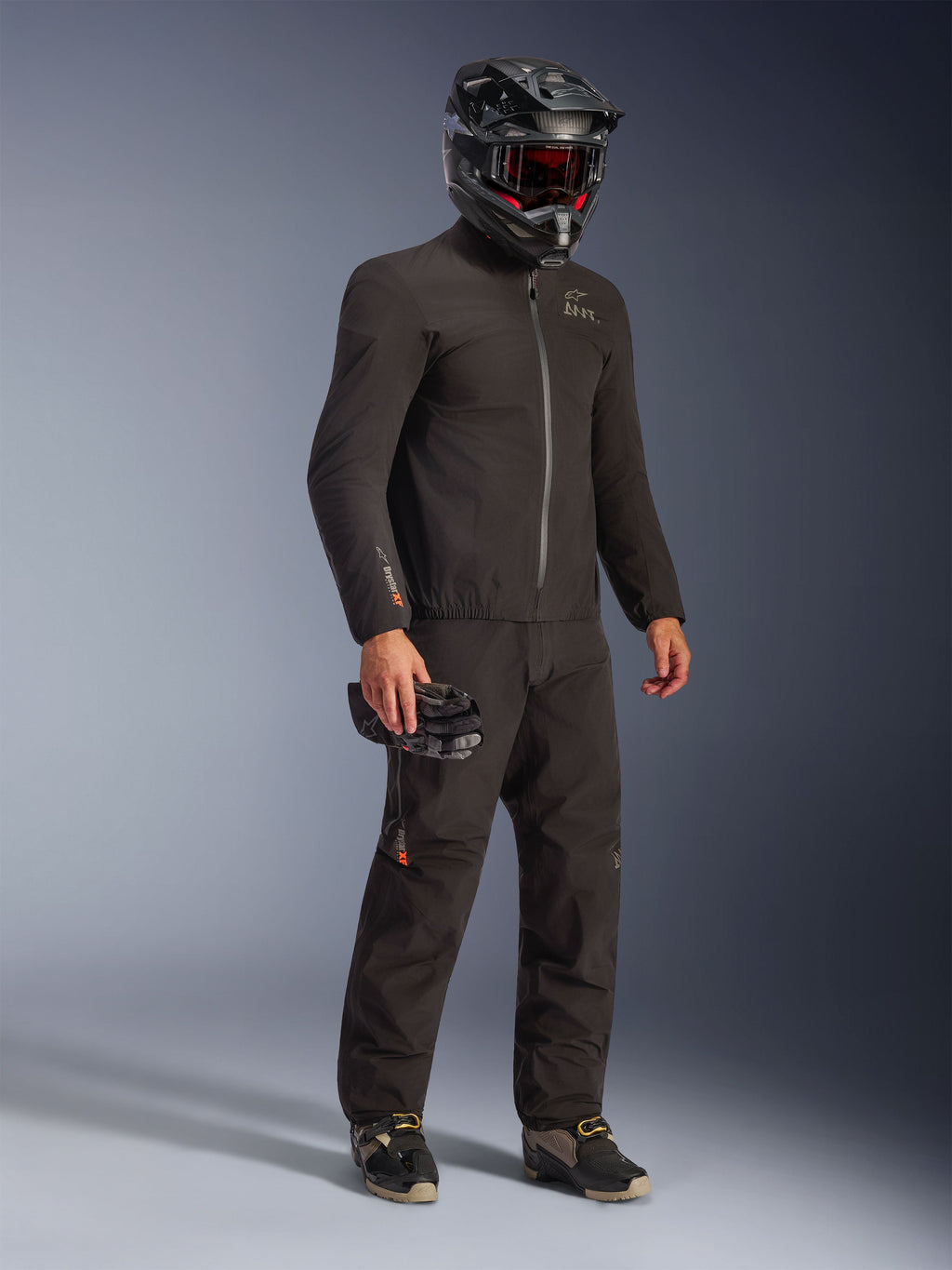 Alpinestars AMT-8 Stretch Drystar® XF Jacket in Black, worn as part of a full riding kit with matching pants and a black helmet, featuring a sleek textile design with orange Drystar XF branding on the sleeve, ideal for adventure touring.