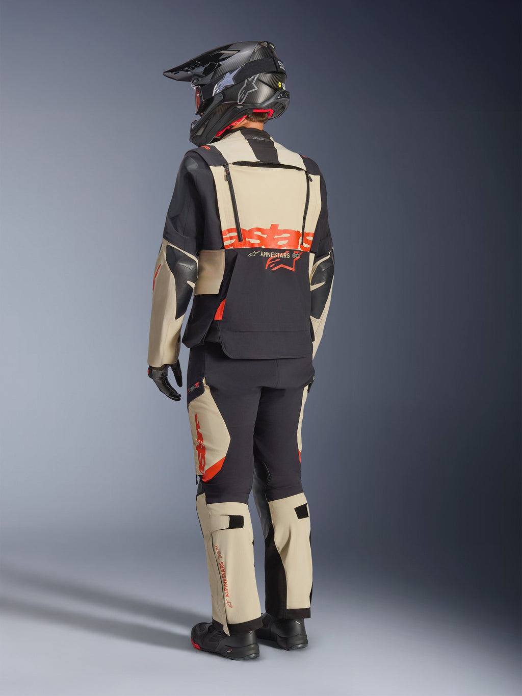 Alpinestars Halo Pro Drystar® XF Laminierte Jacke, Mastic Black, Rückansicht eines Fahrers im kompletten Adventure-Motorradanzug mit passender Hose, schwarzem Adventure-Helm und Stiefeln, mit einem markanten roten Alpinestars-Logo auf dem Rücken.
