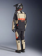 Alpinestars Halo Pro Drystar® XF Laminierte Jacke, Mastic Black, Rückansicht eines Fahrers im kompletten Adventure-Motorradanzug mit passender Hose, schwarzem Adventure-Helm und Stiefeln, mit einem markanten roten Alpinestars-Logo auf dem Rücken.