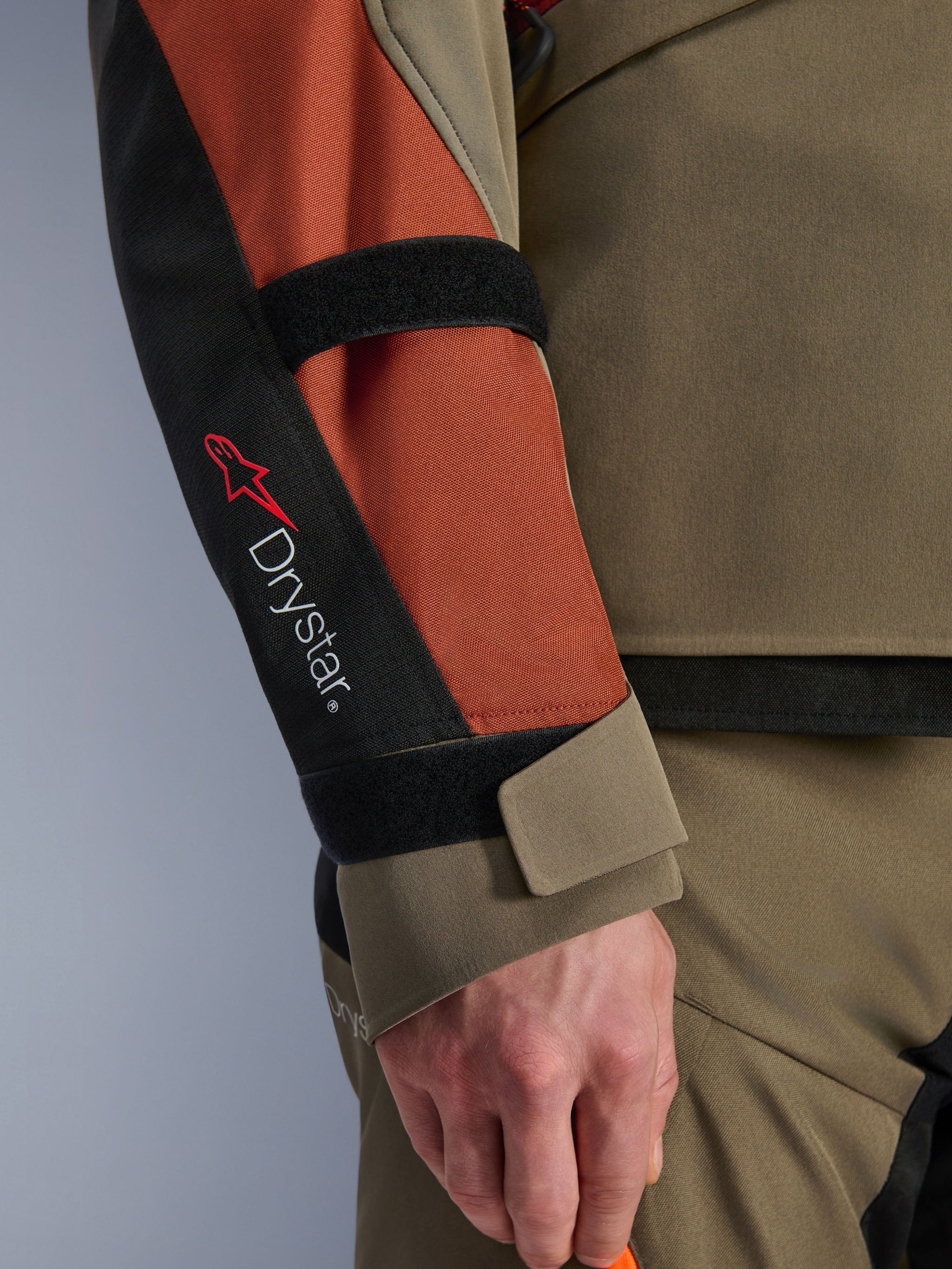 Alpinestars Andes V4 Drystar® Jacket, Motorcycle Jacket, Walnut Rust Black, close-up view of the sleeve with Drystar® branding and red star logo, featuring adjustable forearm and wrist velcro straps, durable adventure touring textile design