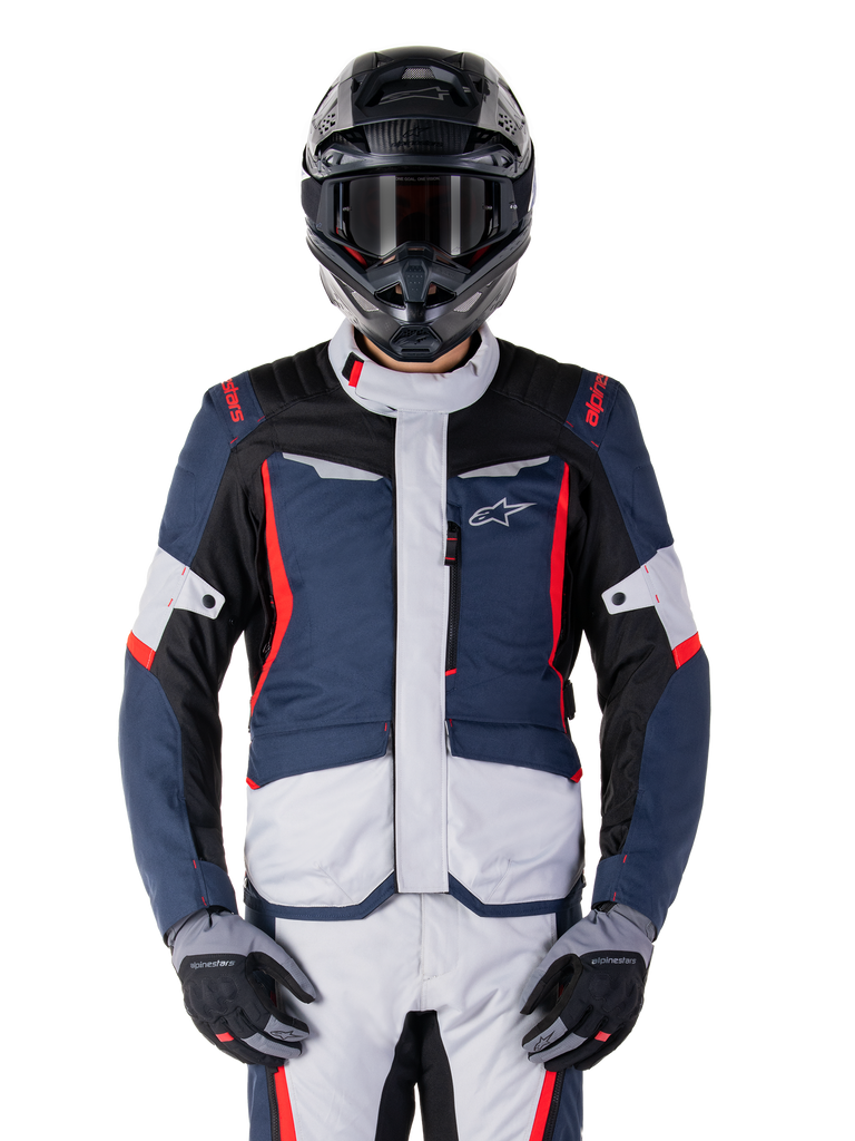 Alpinestars ST-1 wasserdichte Jacke, Adventure-Tourenjacke, Dunkelblau, Schwarz und leuchtendes Rot, getragen mit einem schwarzen Adventure-Helm und grauen Handschuhen, mit hellgrauen Einsätzen und roten Akzenten an Schultern und Reißverschlüssen, schlankes Design mit Alpinestars-Branding auf der Brust, strapazierfähige wasserdichte Ausrüstung zum Motorradfahren