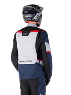 Alpinestars ST-1 Waterproof Jacket, Dark Blue Black and Bright Red, back view on a rider wearing a black adventure helmet, featuring light gray panels and Alpinestars branding, adventure touring motorcycle gear