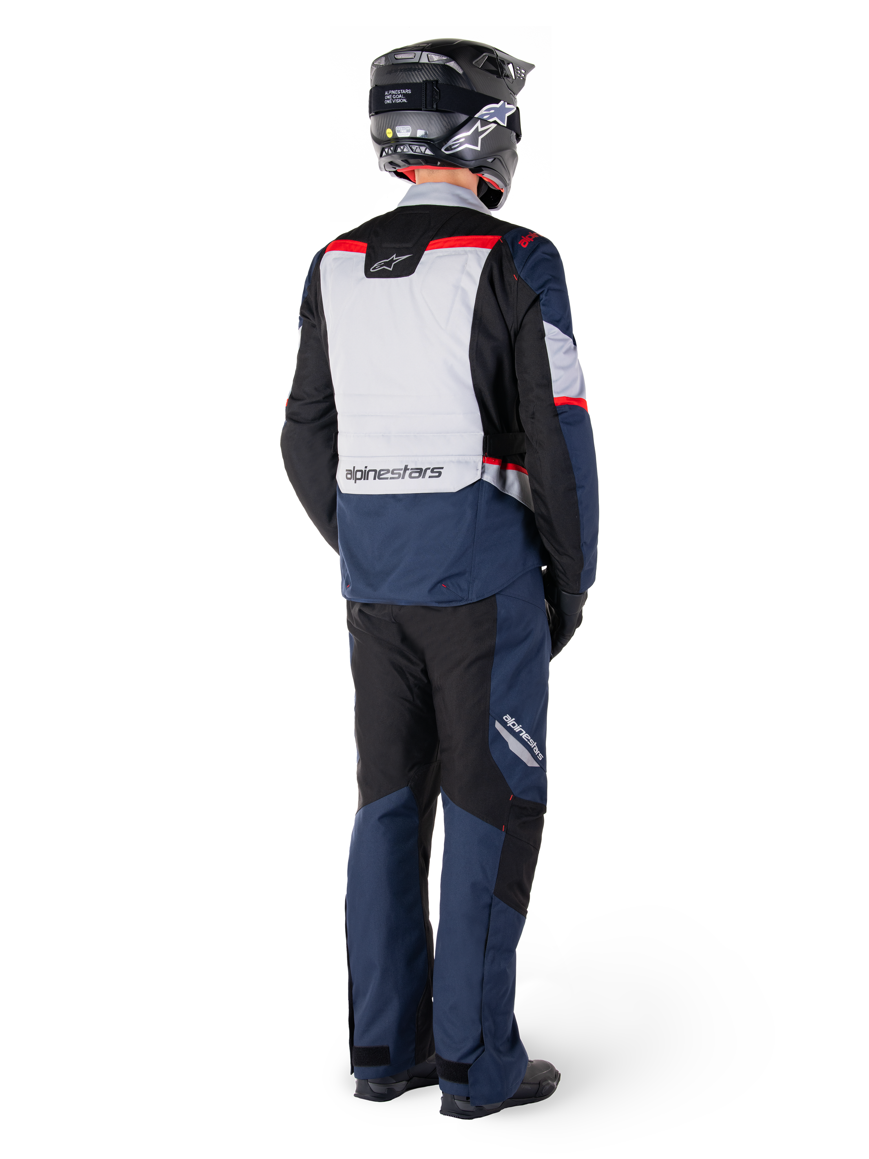 Rear view of a rider wearing the Alpinestars ST-1 Waterproof Jacket in Dark Blue Black Bright Red, paired with matching waterproof pants and a black helmet, featuring a prominent grey back panel with Alpinestars branding and an adventure touring design.