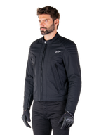 Alpinestars Clayton WR Jacke, Schwarz, urbane Textil-Motorradjacke mit gesteppten Schulter- und Unterarmdetails, schmale Passform, mattes Finish, getragen von einem Fahrer mit schwarzen Handschuhen.