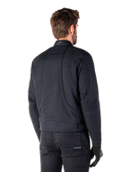 Alpinestars Clayton WR Jacke in Schwarz, Rückansicht in Dreiviertel-Perspektive an einem männlichen Model, urbane Motorradjacke mit gesteppten Polsterungen an Schultern und Ellbogen, technischen Stepplinien und reflektierendem Logo am Kragen, kombiniert mit schwarzer Hose und Handschuhen.