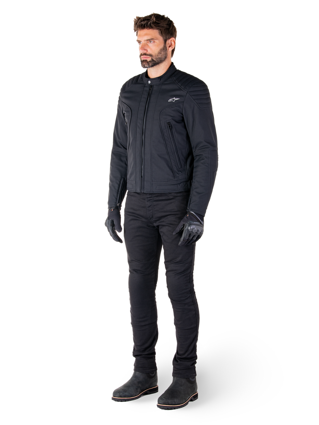 Männlicher Fahrer in der Alpinestars Clayton WR Jacke, schwarze Urban-Motorradjacke, Slim-Fit-Design mit gesteppten Schulterakzenten und mattem Finish, kombiniert mit schwarzer technischer Motorradhose und Handschuhen.